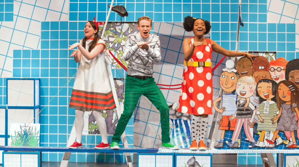 3 people stand on a colorful set, singing and dancing